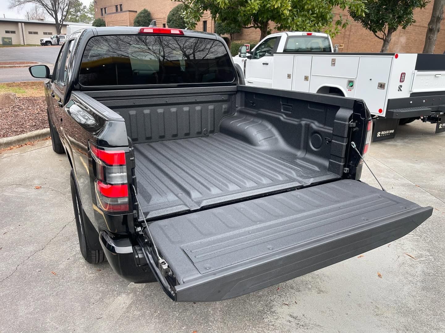 Black pickup truck bed with tailgate open, parked outdoors.