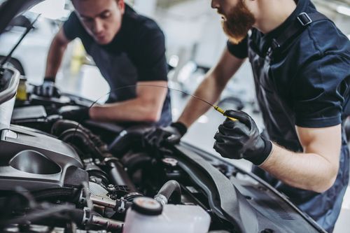 Mechanics inspecting a car engine in a garage, one using a diagnostic tool.