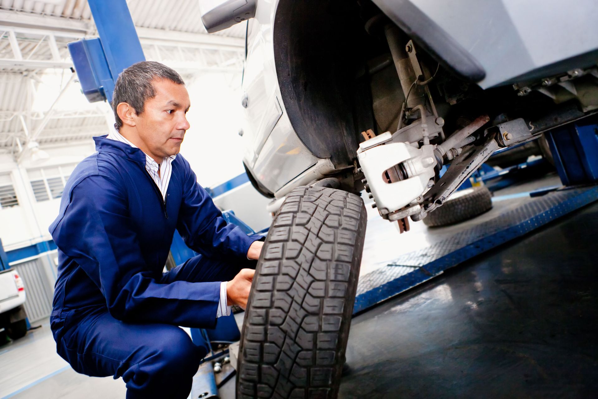 Mechanic inspecting a car’s front wheel on a lift in an auto repair shop