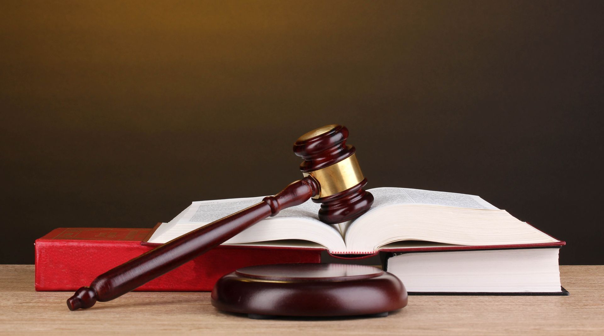 Wooden gavel on open law book, resting on a stack of books, in front of a dark background.