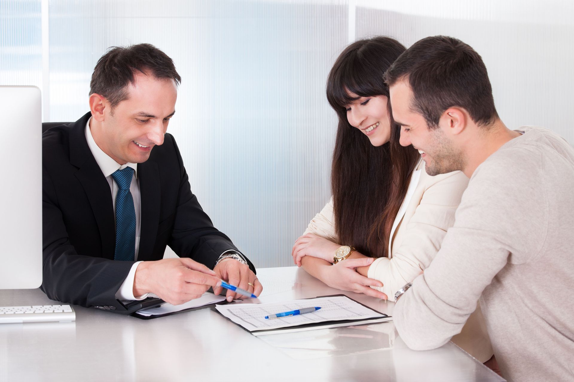 A financial advisor reviewing paperwork with a smiling couple at a desk.