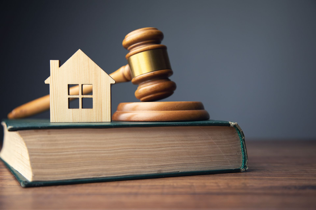 Wooden house figurine, gavel, and book on a wooden surface, symbolizing real estate law.