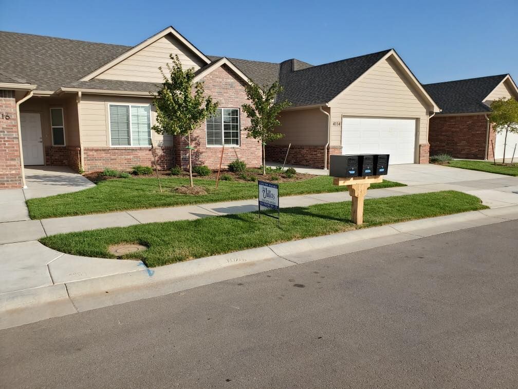 Row of beige houses with brick accents, green lawns, and mailboxes on a sunny day.