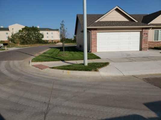 A townhouse with a white garage door on a sunny day. A tree and a street are visible.