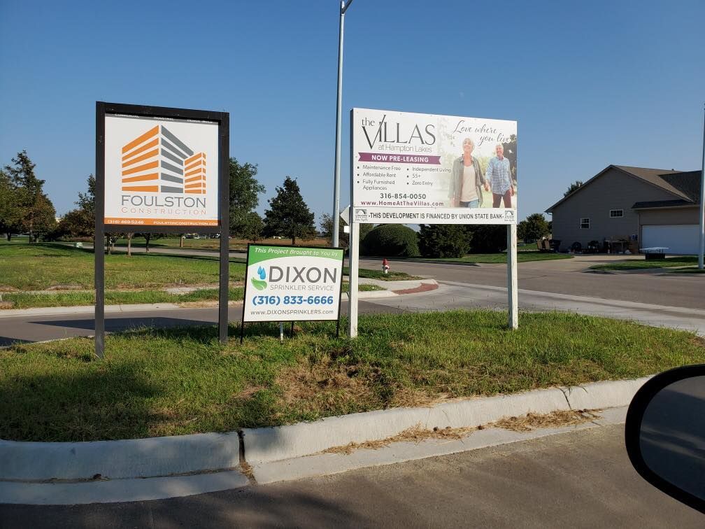 Signs for Poulston and Villas, Dixon Real Estate, on grassy median near a road.