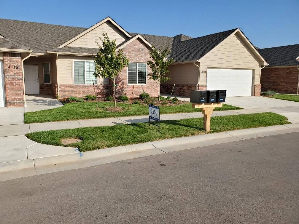 Townhouse exterior with brick and beige siding, green lawn, and mailboxes on a sunny day.