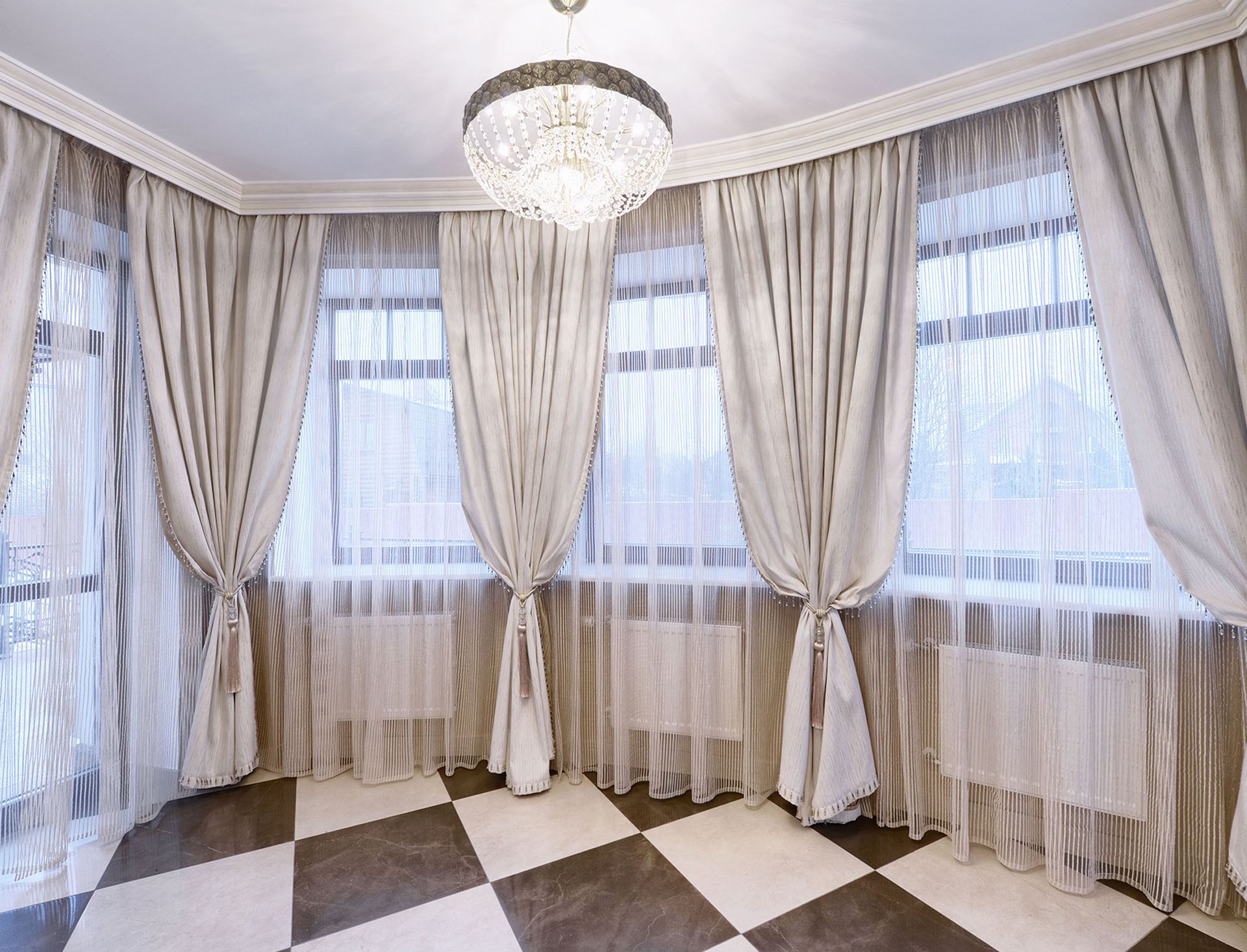 A room with a checkered floor , curtains , and a chandelier.