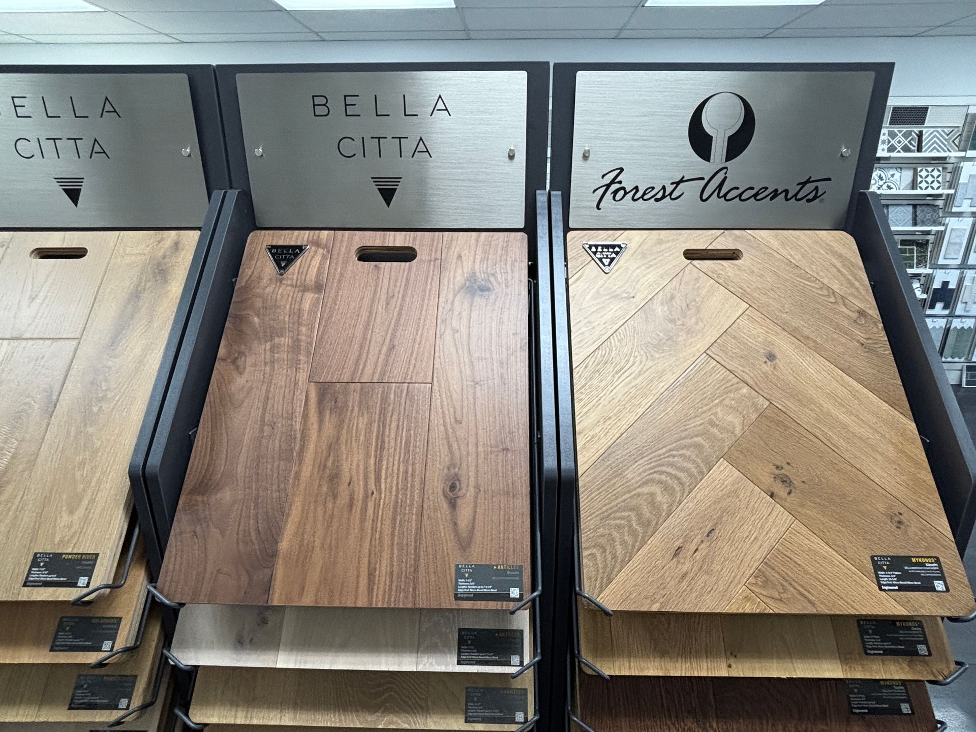 Display of wood flooring samples, including Bella Citta and Forest Accents brands, in a store setting.