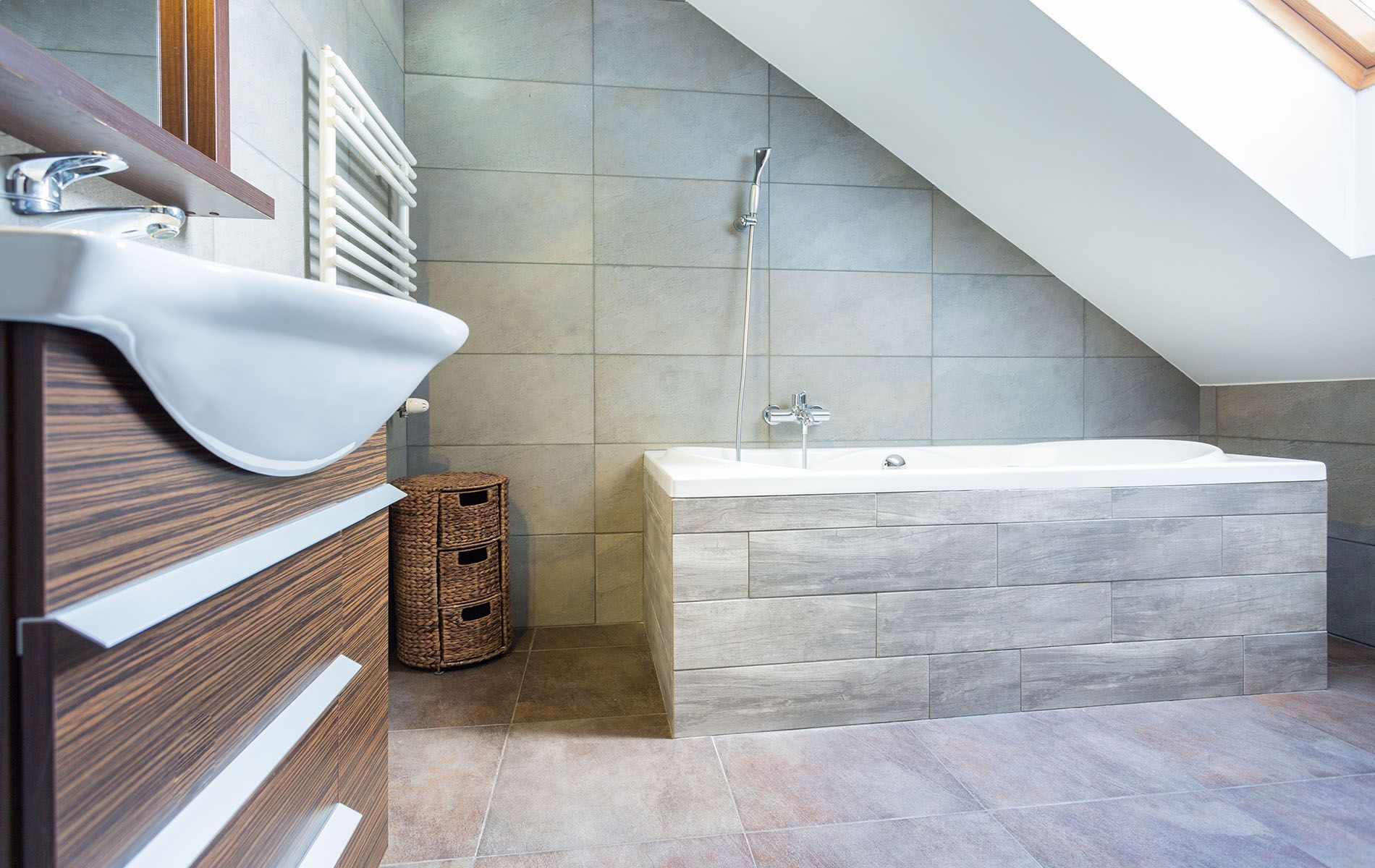 A bathroom with a bathtub , sink , mirror and skylight.
