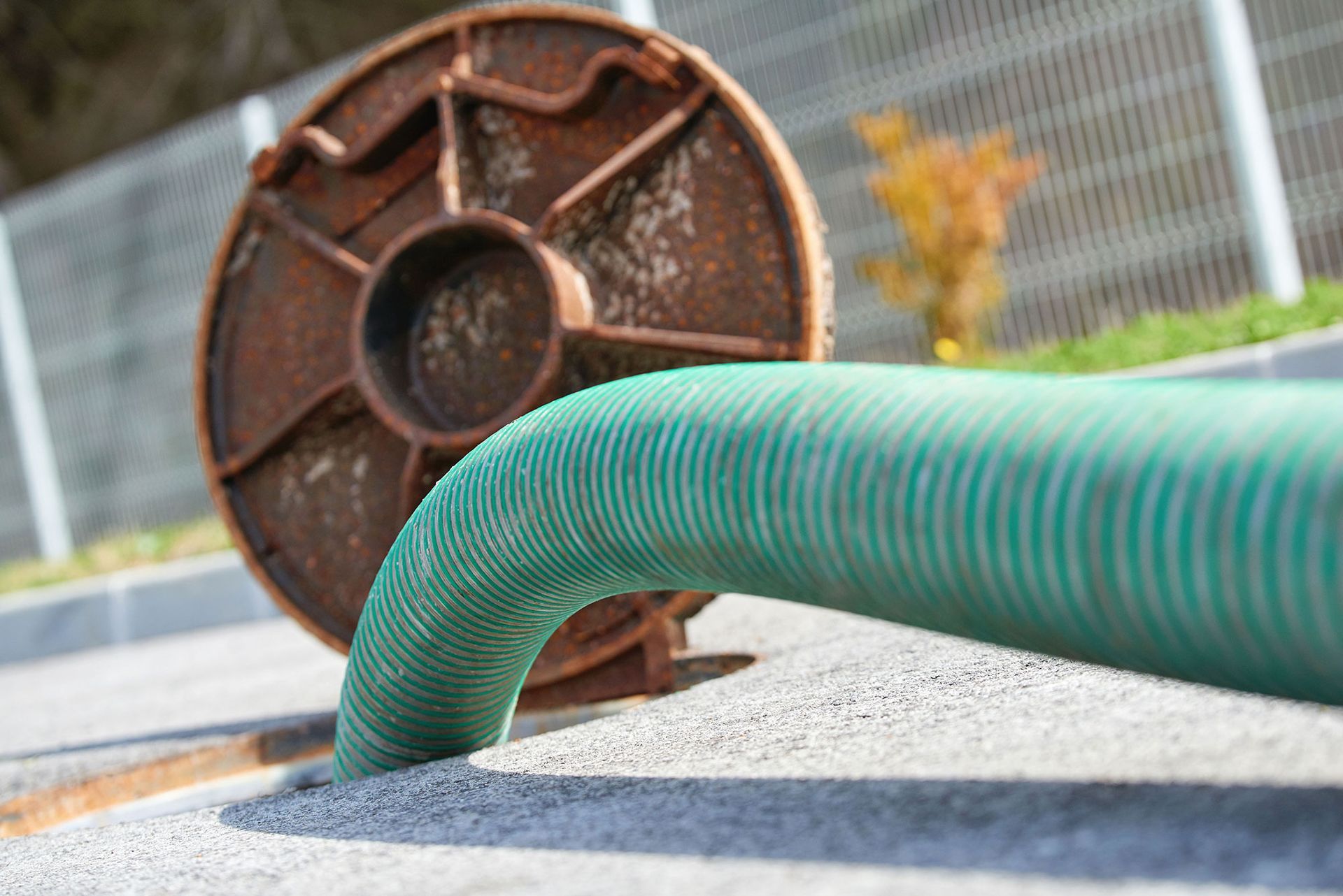 Green hose extending from a rusty metal spool on concrete.