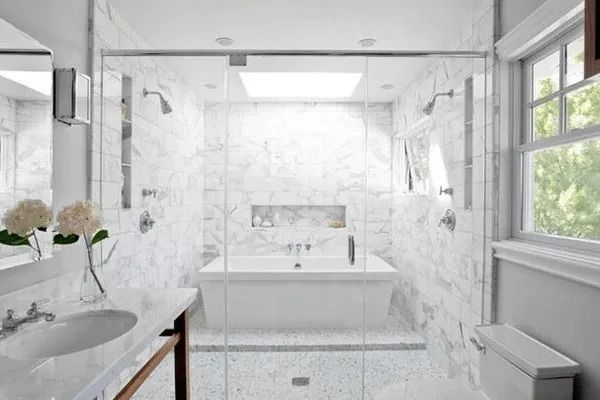 Elegant white marble bathroom with a bathtub, shower, and window.