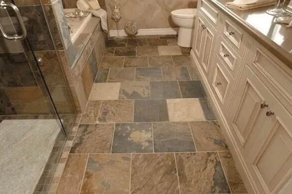 Bathroom with slate tile flooring, off-white vanity, and glass shower door.