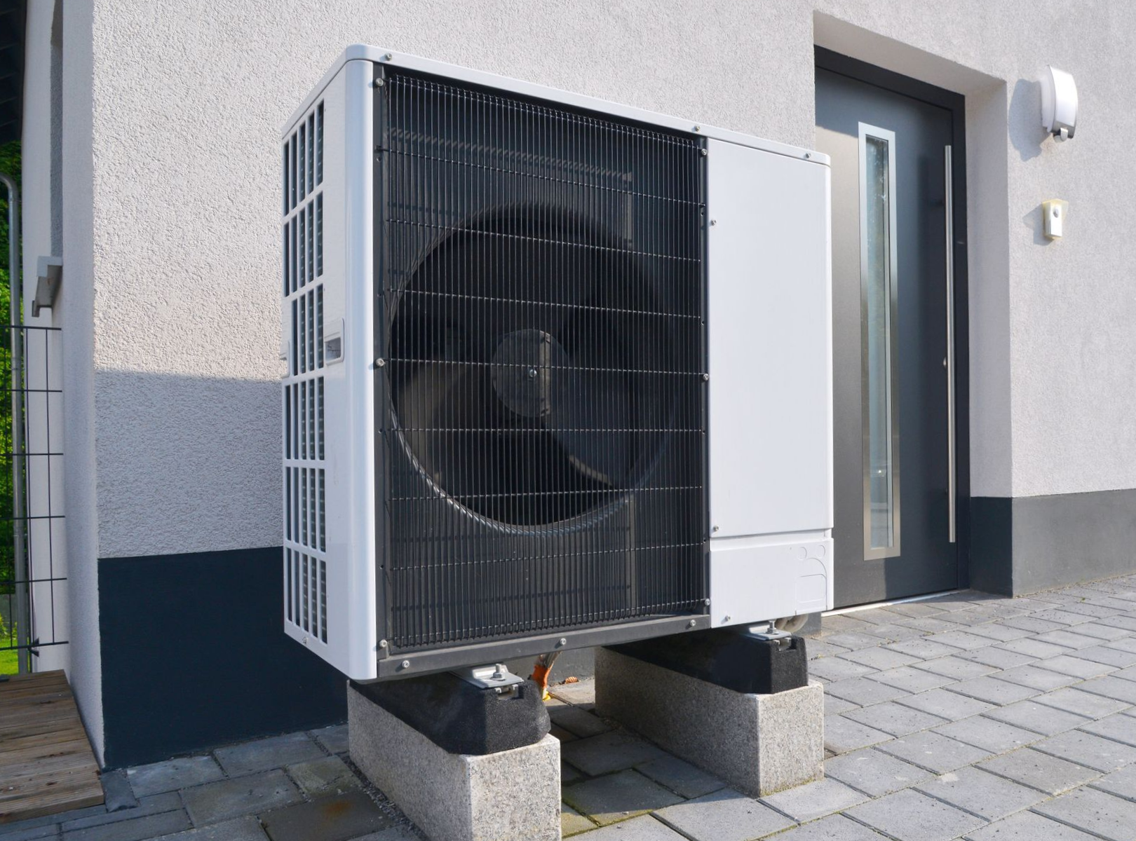 Heat pump unit mounted on concrete blocks outside a house.