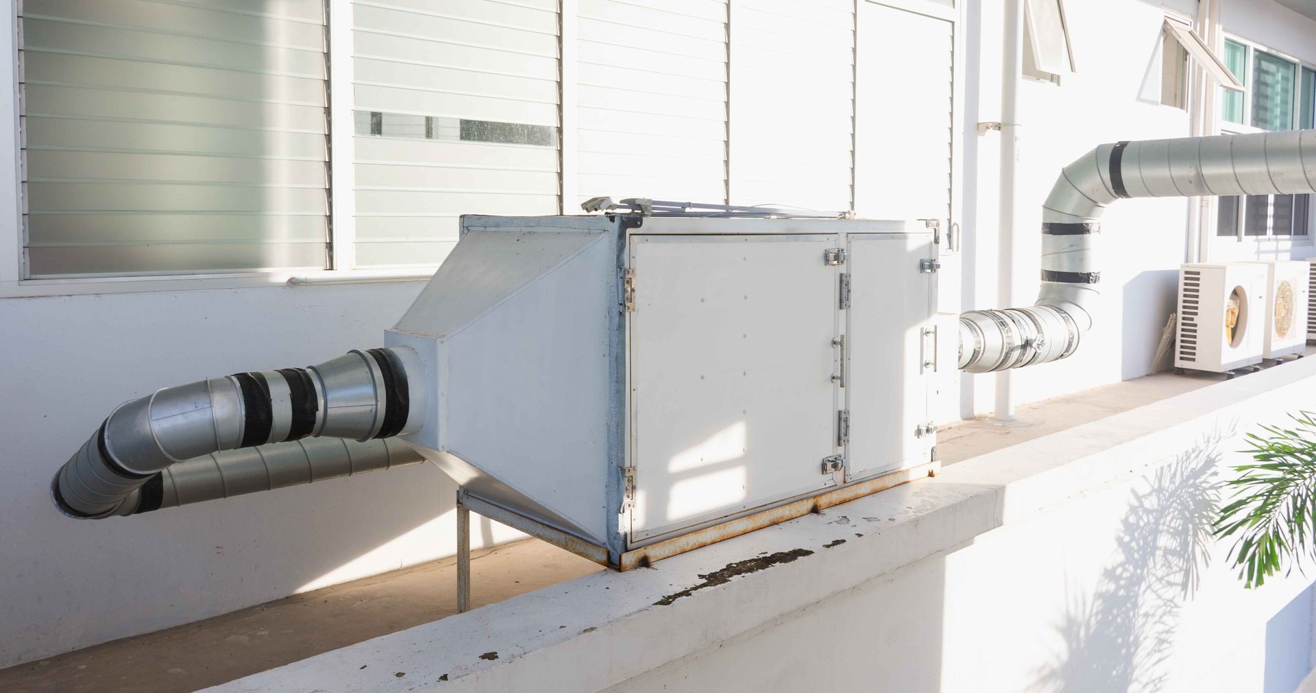 Metal HVAC unit on a building's exterior wall, connected to ducts.