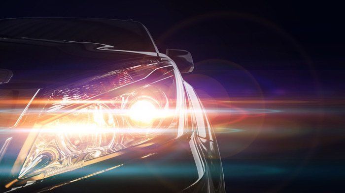 A car headlight illuminates against a dark background, with lens flares.