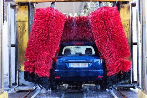 Blue car being washed in a car wash with large, red brushes.