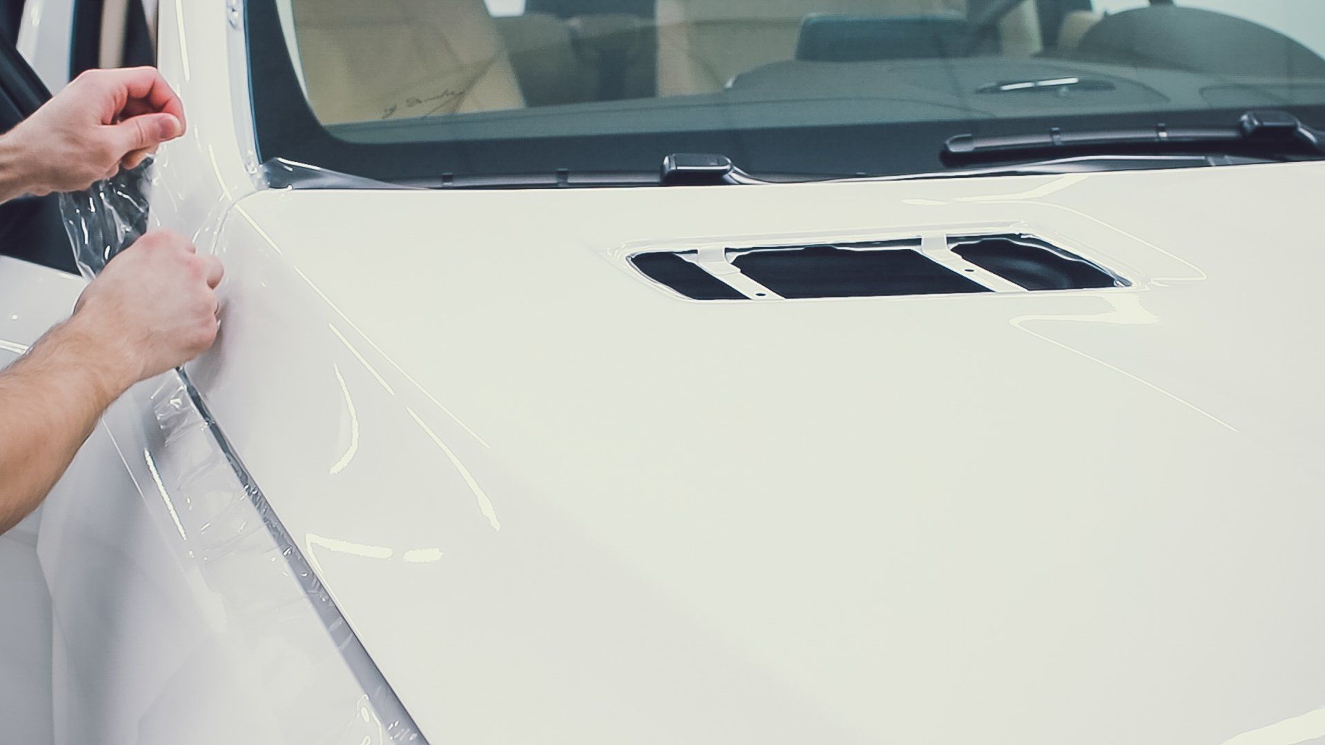 Person applying protective film to the hood of a white car.