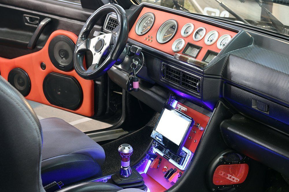 Customized car interior with orange speaker panels, gauges, and a silver steering wheel.