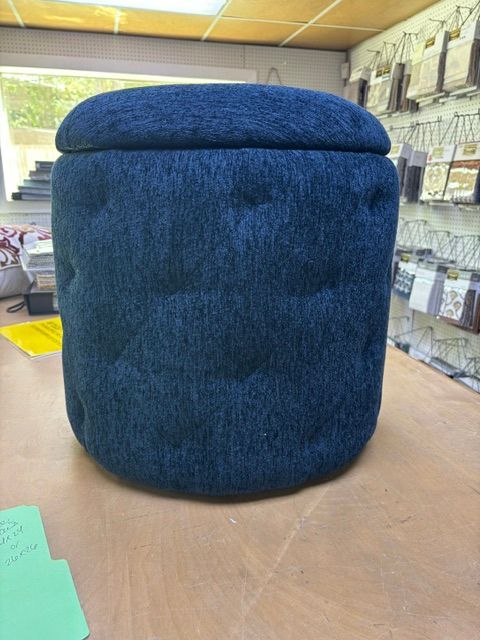 Blue upholstered ottoman on a wooden table in a store aisle.