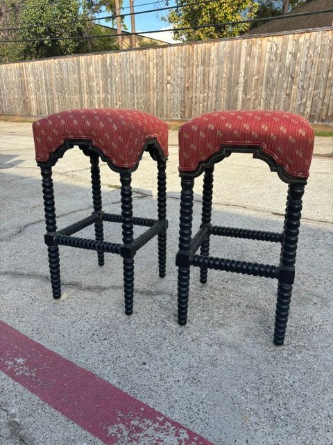 Two red upholstered bar stools with black beaded legs on a concrete driveway outdoors