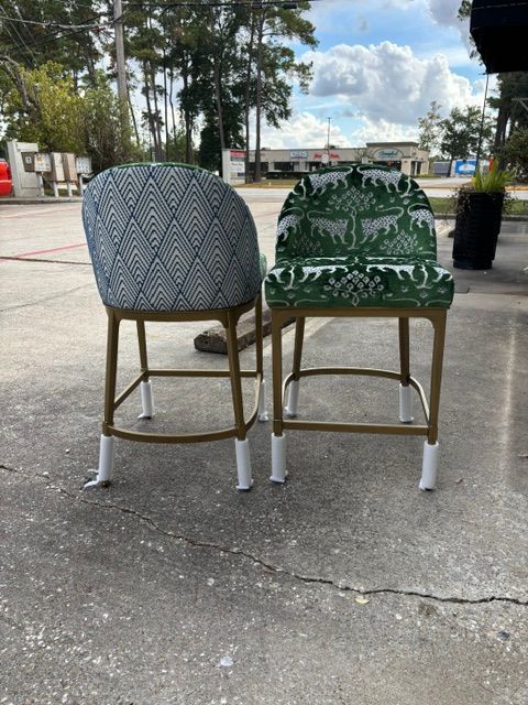 Two patterned chairs on a paved outdoor area, one gray and one green, viewed from behind.