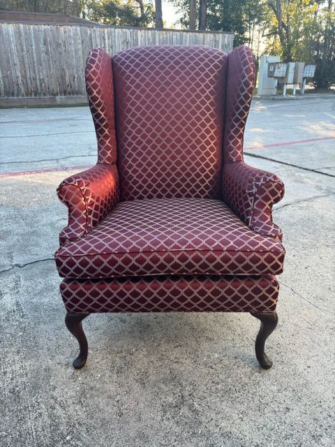 Red patterned wingback armchair on a concrete driveway outdoors, with wooden fence in the background