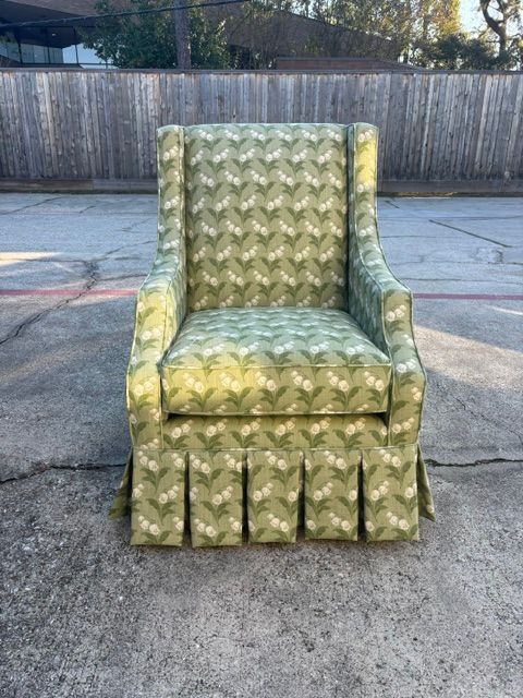 Green patterned armchair centered on a concrete outdoor surface with a fence in the background