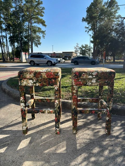 Two weathered chairs in the foreground, with a parking lot, cars, and trees in sunlight behind them.