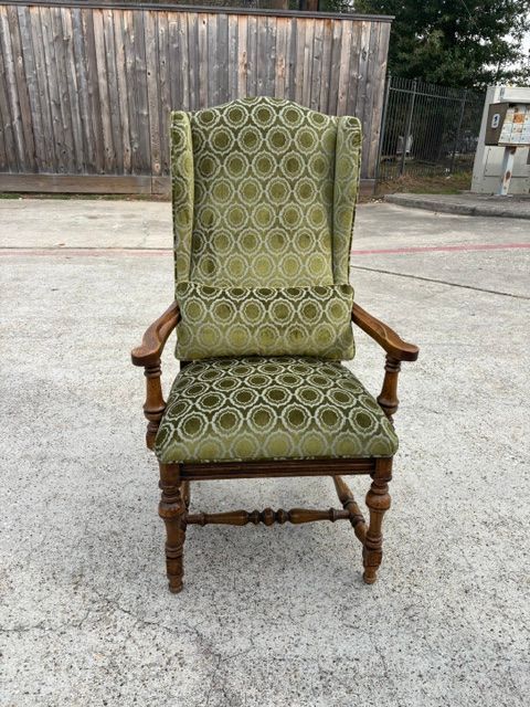 Green patterned wingback armchair with wooden arms and legs, centered on a concrete surface outdoors