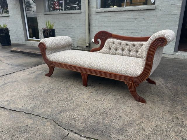 Antique tufted cream and wood loveseat on a concrete driveway outside a house