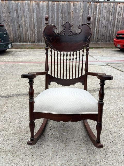 Vintage dark wood rocking chair with white upholstered seat on a concrete surface outdoors