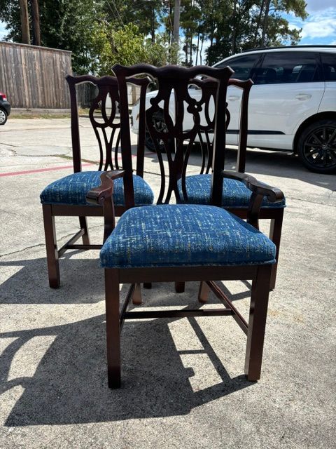 Two wooden chairs with blue seats on a sunlit driveway, with a white car in the background