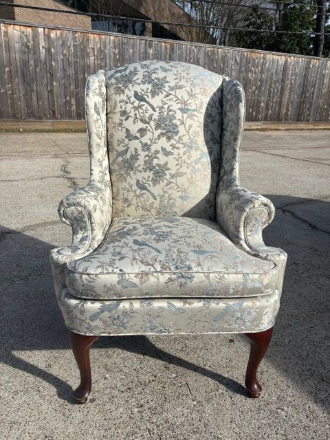 Vintage upholstered armchair with floral fabric and wooden legs, sitting outdoors on pavement.