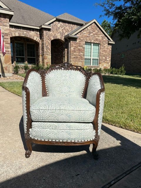 Vintage upholstered armchair on a driveway in front of a brick house on a sunny day