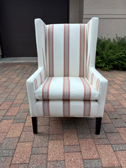 White upholstered wingback chair with striped fabric, standing on a brick patio.