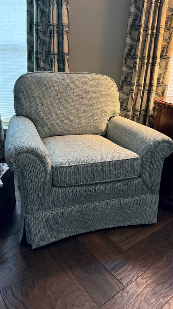 Gray upholstered armchair by a window with patterned curtains on a dark wood floor