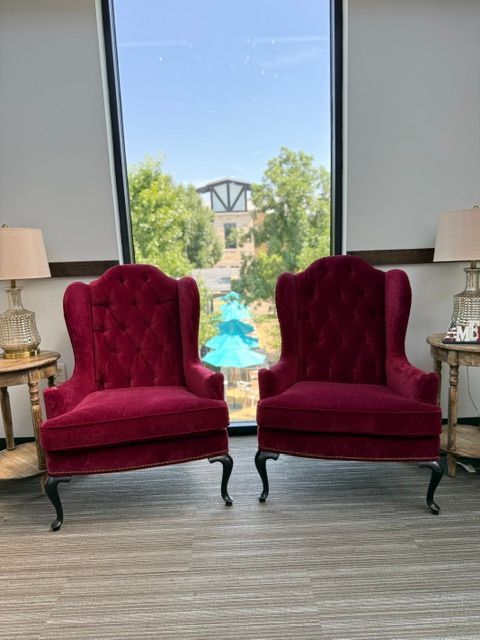 Two burgundy velvet armchairs facing a window with a pool and garden view