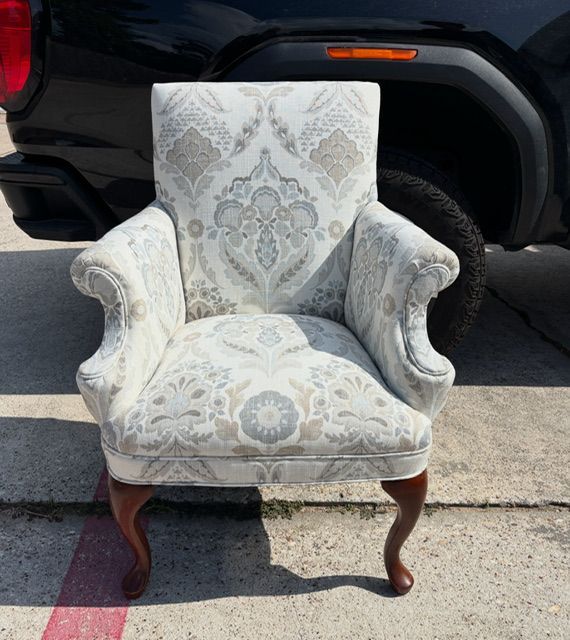 Vintage white upholstered armchair with gray damask pattern sitting on a driveway in front of a vehicle.