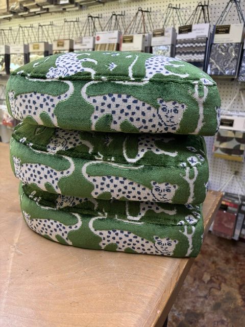Stacked green patterned fabric bundles on a table in a store aisle.