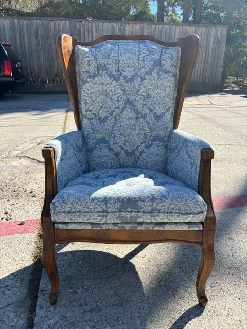 Blue upholstered wooden armchair on pavement in outdoor parking lot, with a white cushion on the seat