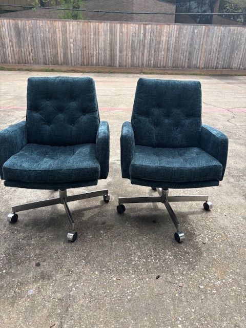 Two teal-colored office chairs with button-tufted backs and chrome bases, set on a concrete surface.