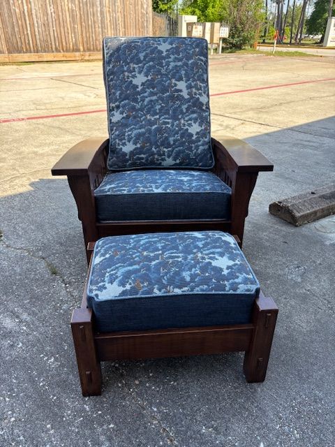Wooden armchair and footstool set with blue floral cushions, set on a concrete surface.