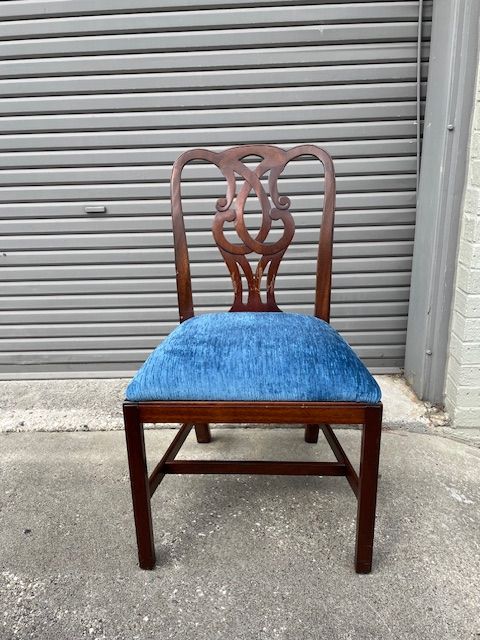 Wooden chair with blue upholstered seat, ornate back, against a gray shutter.