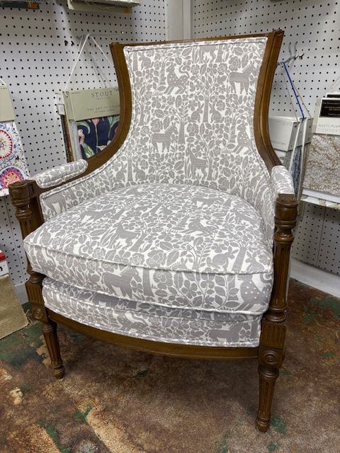 Upholstered armchair with gray patterned fabric, set in front of a pegboard wall with fabric swatches. Wooden frame.