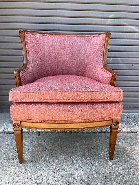 Pink upholstered armchair with wooden frame; set against a gray background.