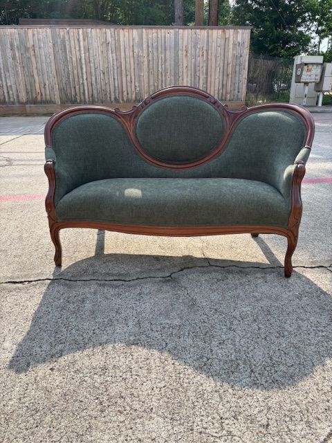 Antique green settee with wooden frame on concrete.