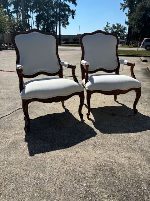 Two white upholstered armchairs with dark wood frames sitting on pavement.