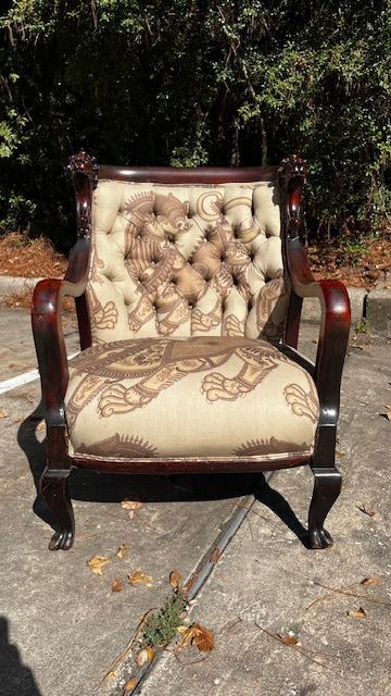 Ornate dark wood armchair with lion-themed upholstery, set outside.