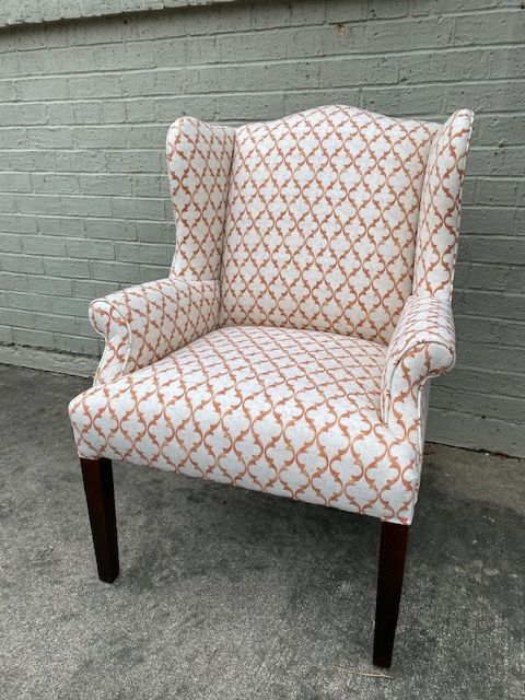 Upholstered wingback chair with cream and orange patterned fabric, dark wooden legs, set outside against a brick wall.