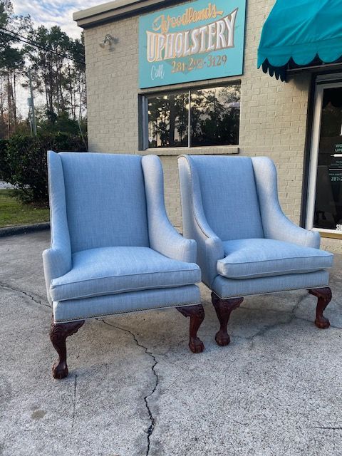 Two light blue upholstered armchairs with dark wood legs in front of an upholstery shop.